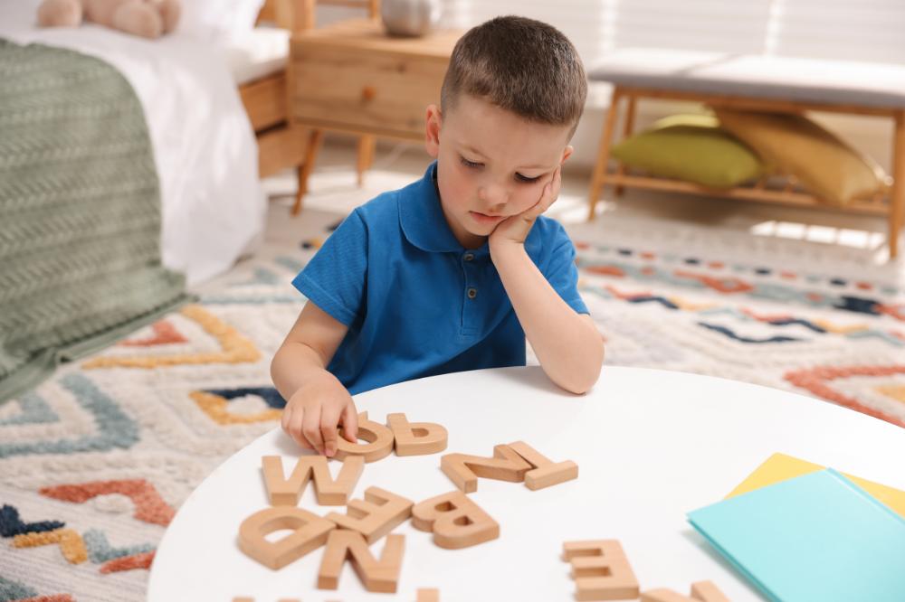 Enfant manipulant des lettres en bois pour apprendre à former des mots, un exercice courant dans l'accompagnement de la dyslexie
